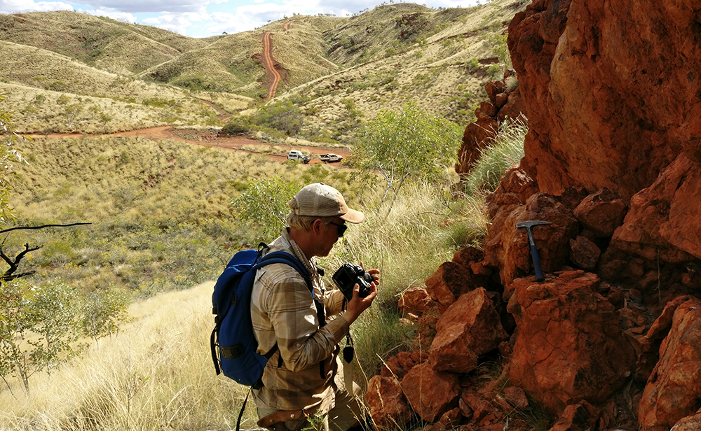 Geologist Benjamin Johnson inspects a rock formation, with grassy hills in the background.