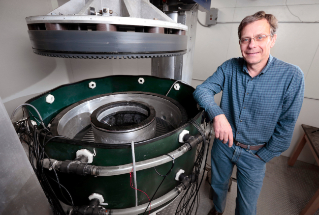 Neal Iverson stands next to large, round metal ring-shear device, which helps study the forces involved in glacier sliding.