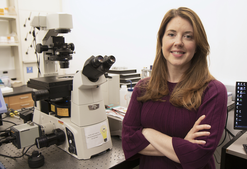 Scientist poses next to microscope