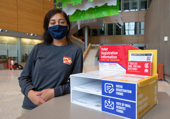 Students leans on table with box display with voter information.