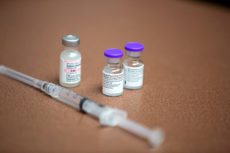 3 vaccine vials and a syringe lie on a table