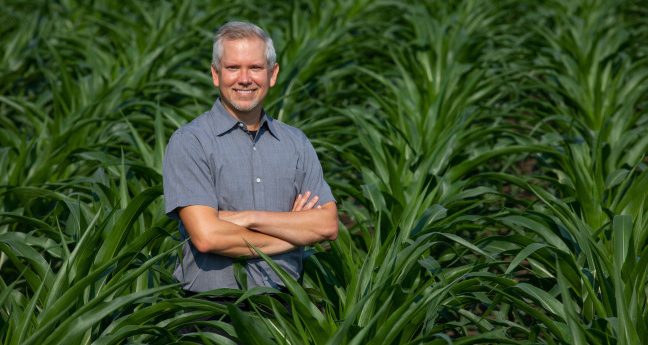 Professor Matthew Hufford stands in a vast cornfield