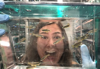 Student smiling behind zebrafish tank.