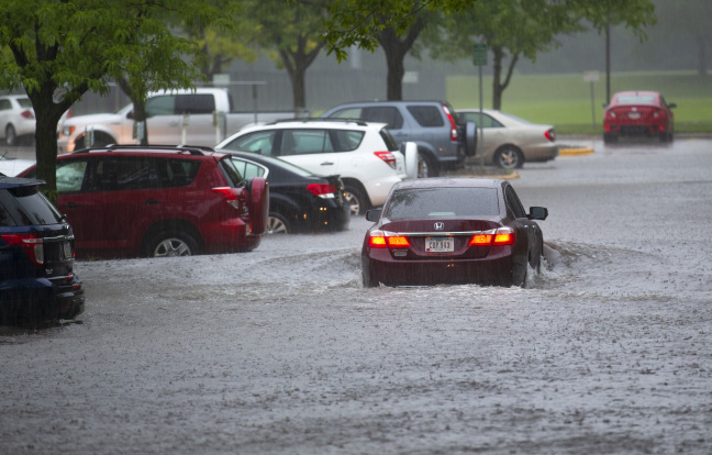 a car wades through deep water in a flooded parking lot