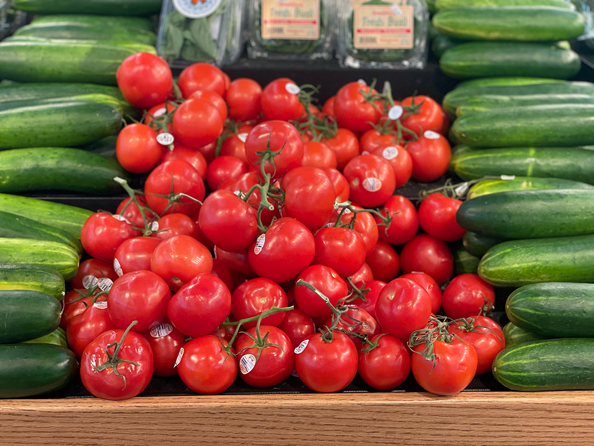 bright red tomatoes and green cucumbers fill a market shelf