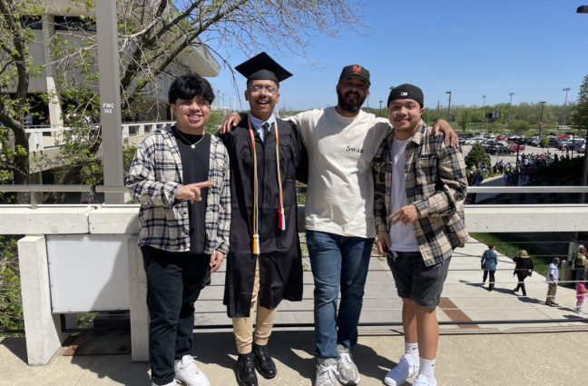 Darrick Burrage poses with friends, wearing his graduation cap and gown.