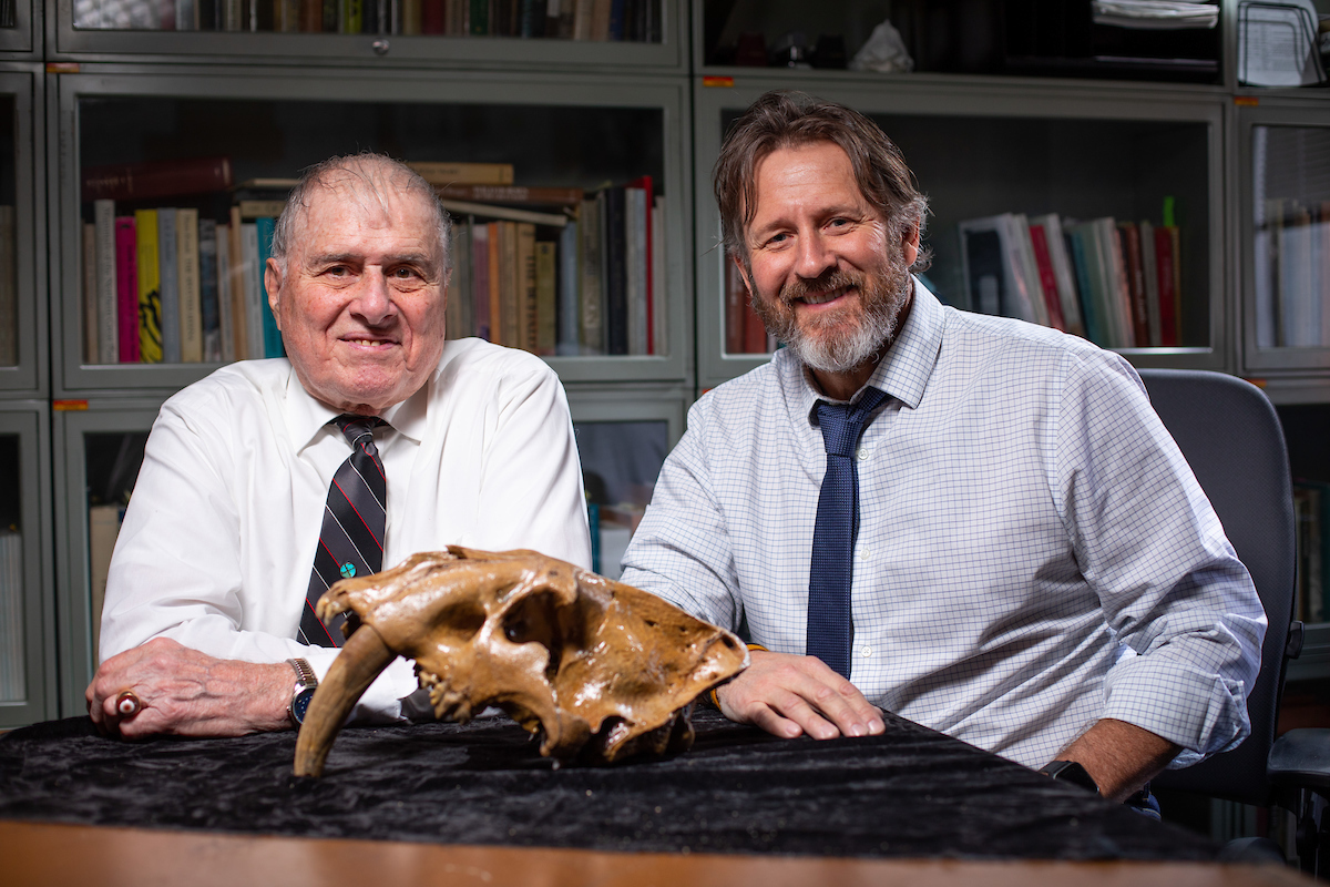 Dave Easterla, Northwest Missouri State, and Matthew Hill, Iowa State, sit with a fossilized complete skull from a sabertooth cat.