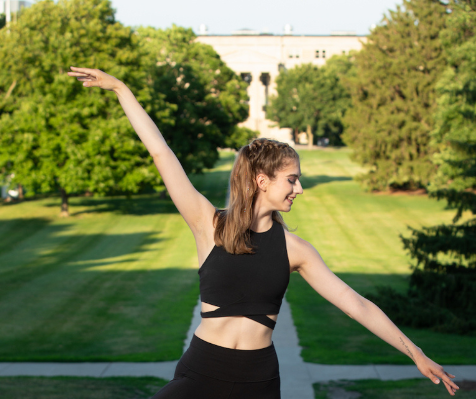 Student strikes dance pose with green campus in background