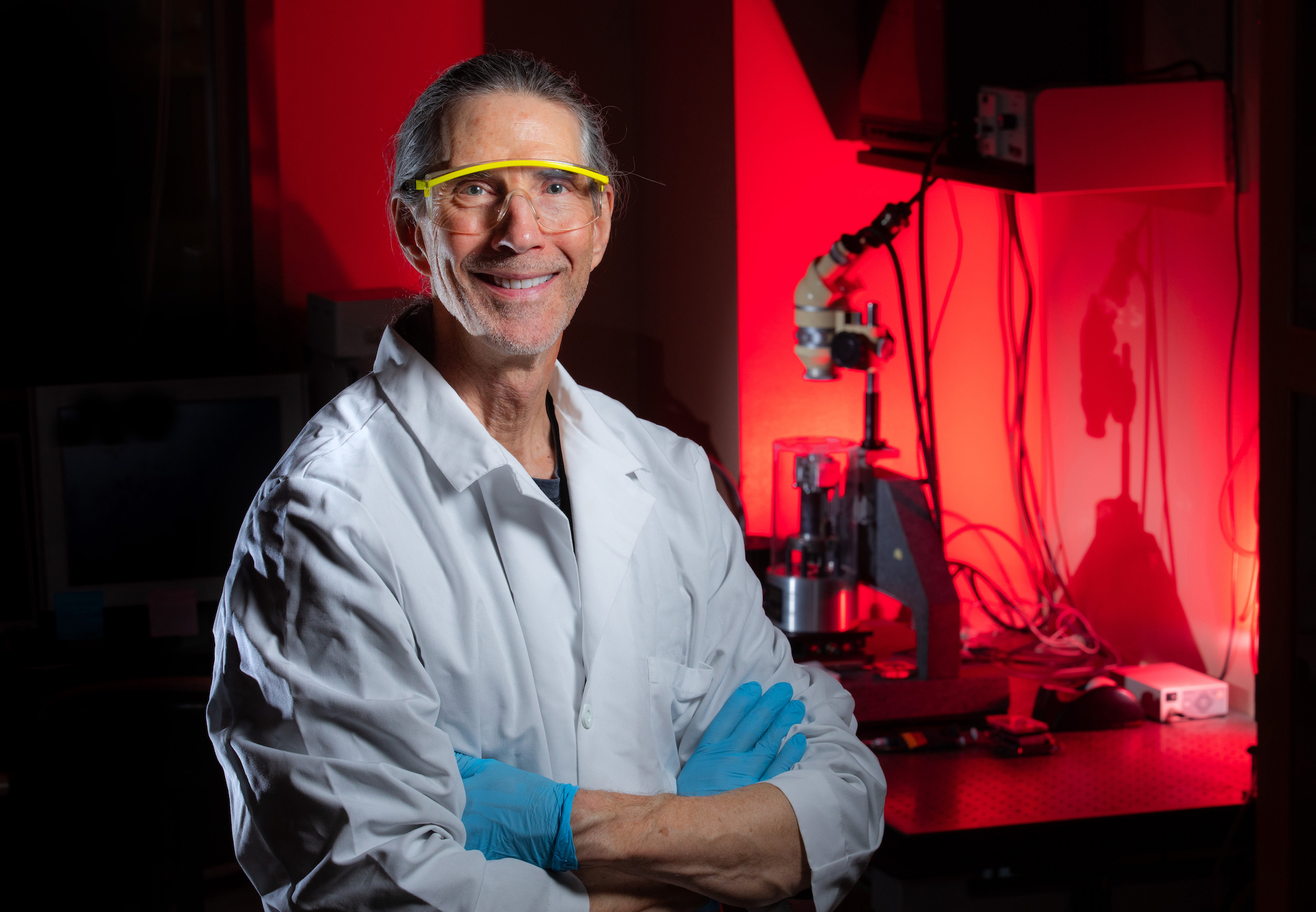 Researcher in white lab coat and blue gloves poses for a portrait