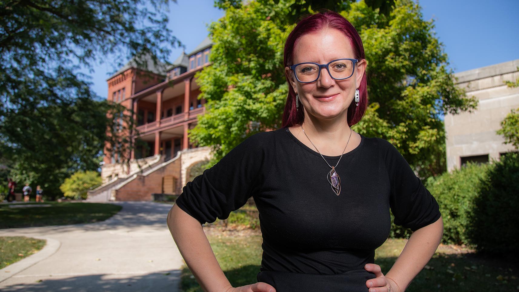 Portrait of Amy Erica Smith outside with trees and the red brick of Catt Hall in the background.