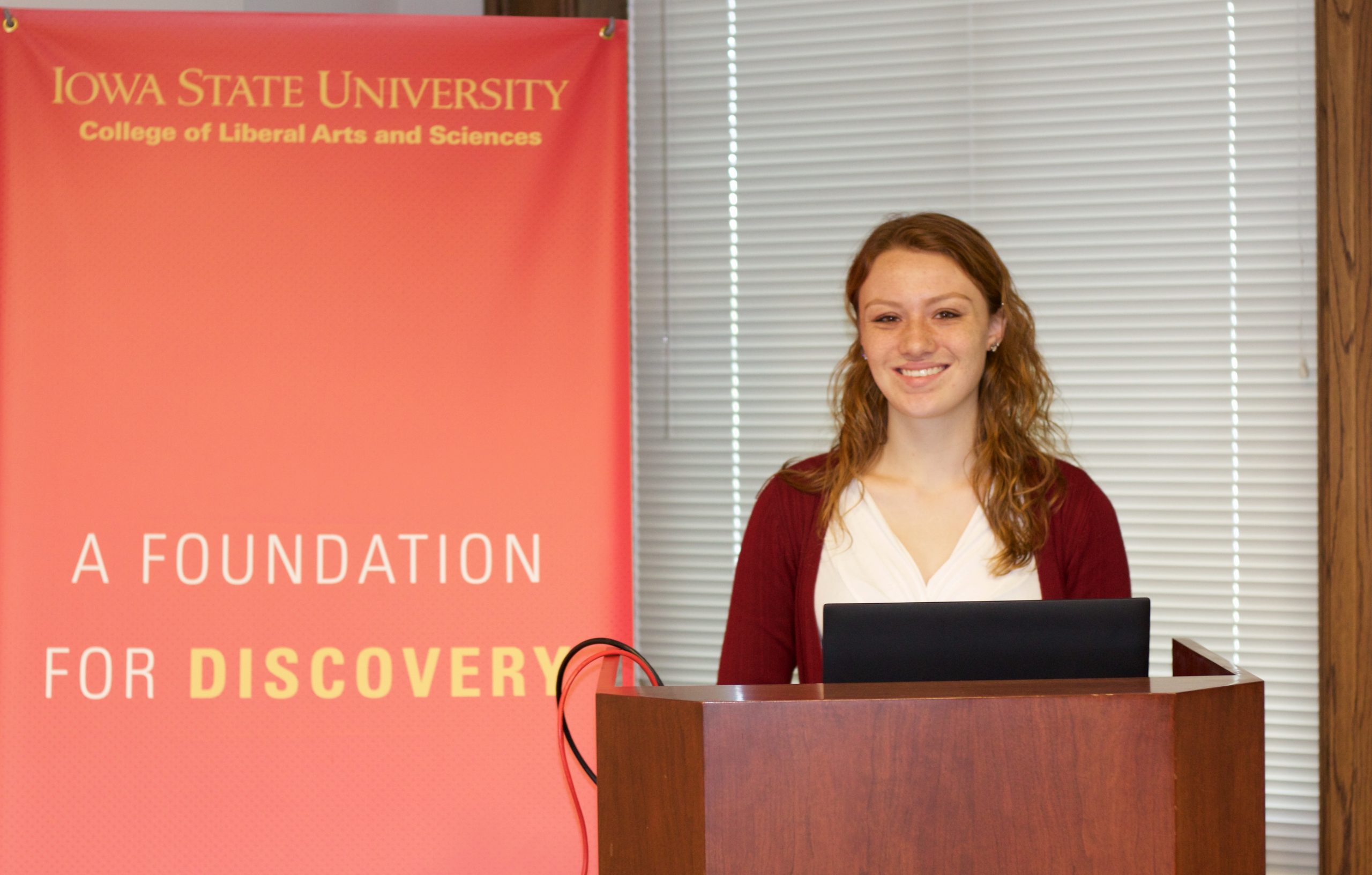 Sonya Haan stands behind a podium in front of a College of Liberal Arts sign, ready to present to university staff.