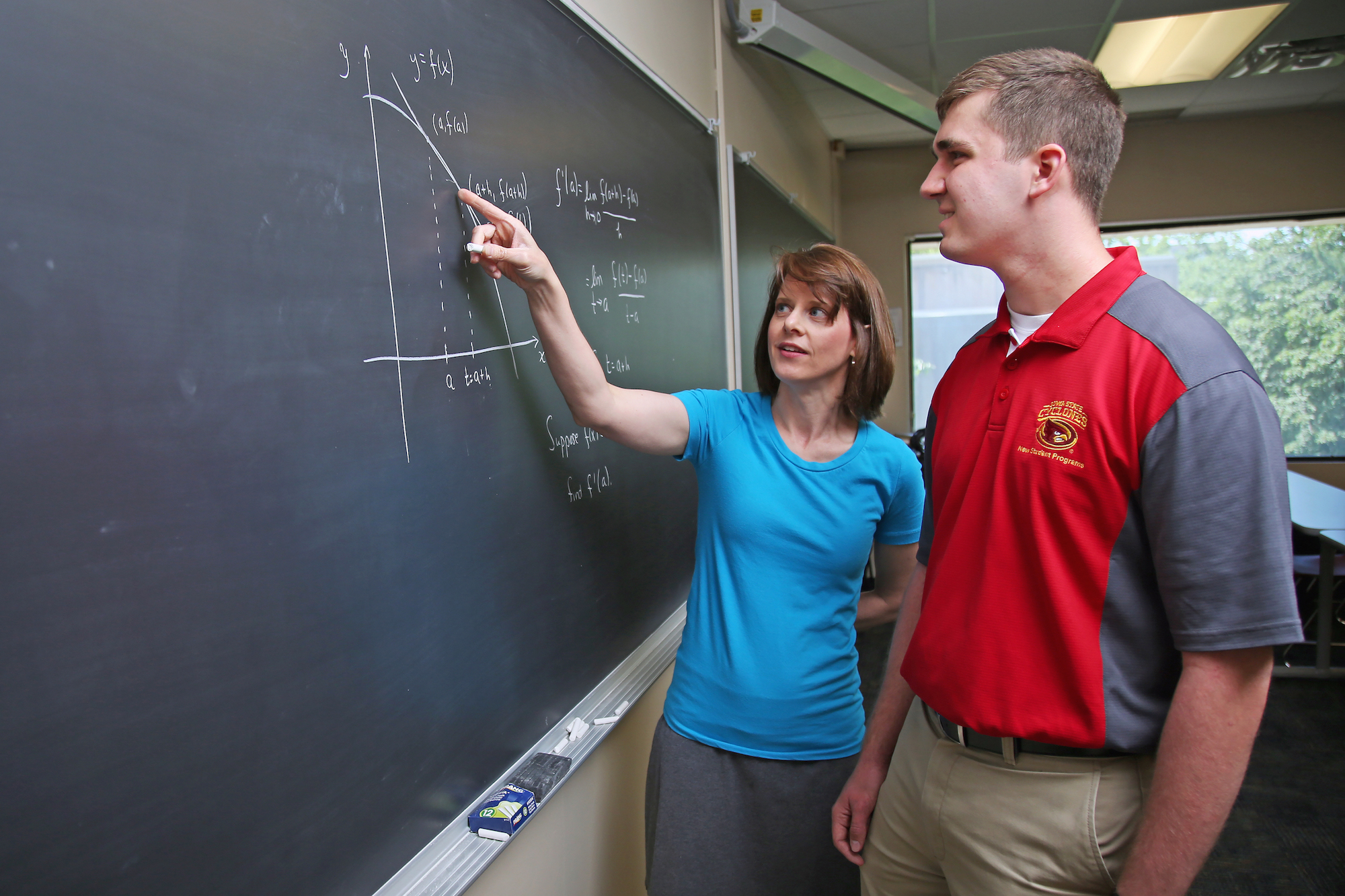 Heather Bolles, senior lecturer in mathematics, stands at a blackboard with a student, explaining the definition of derivative at a point of the graph.