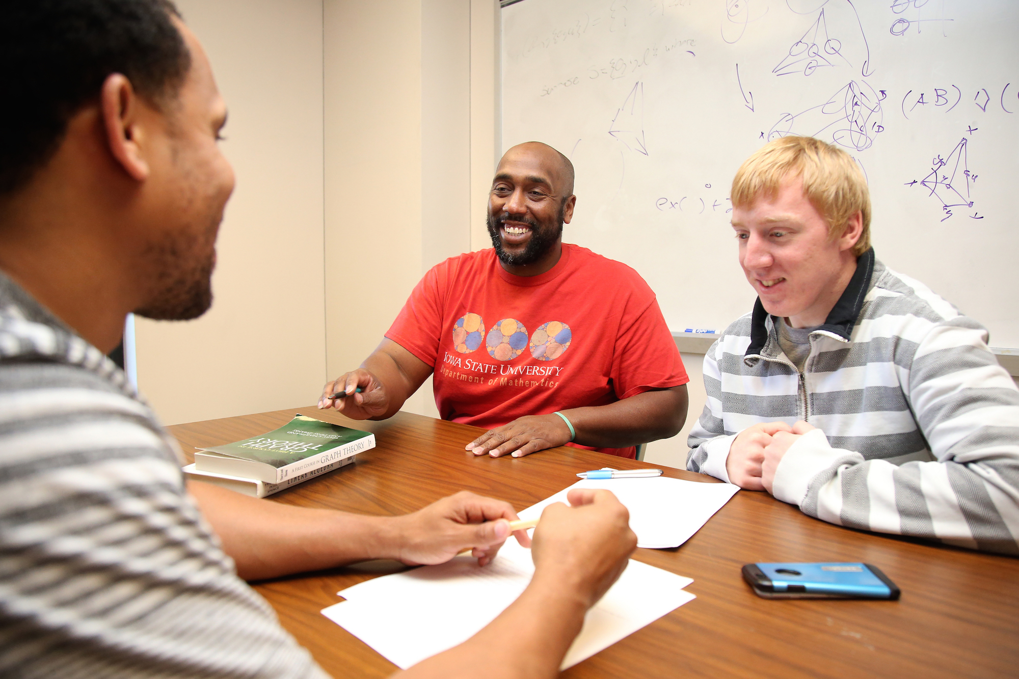 Michael Young, assistant professor of mathematics, in his office at a table working on math problems with graduate students Derek Young and Alex Schulte.