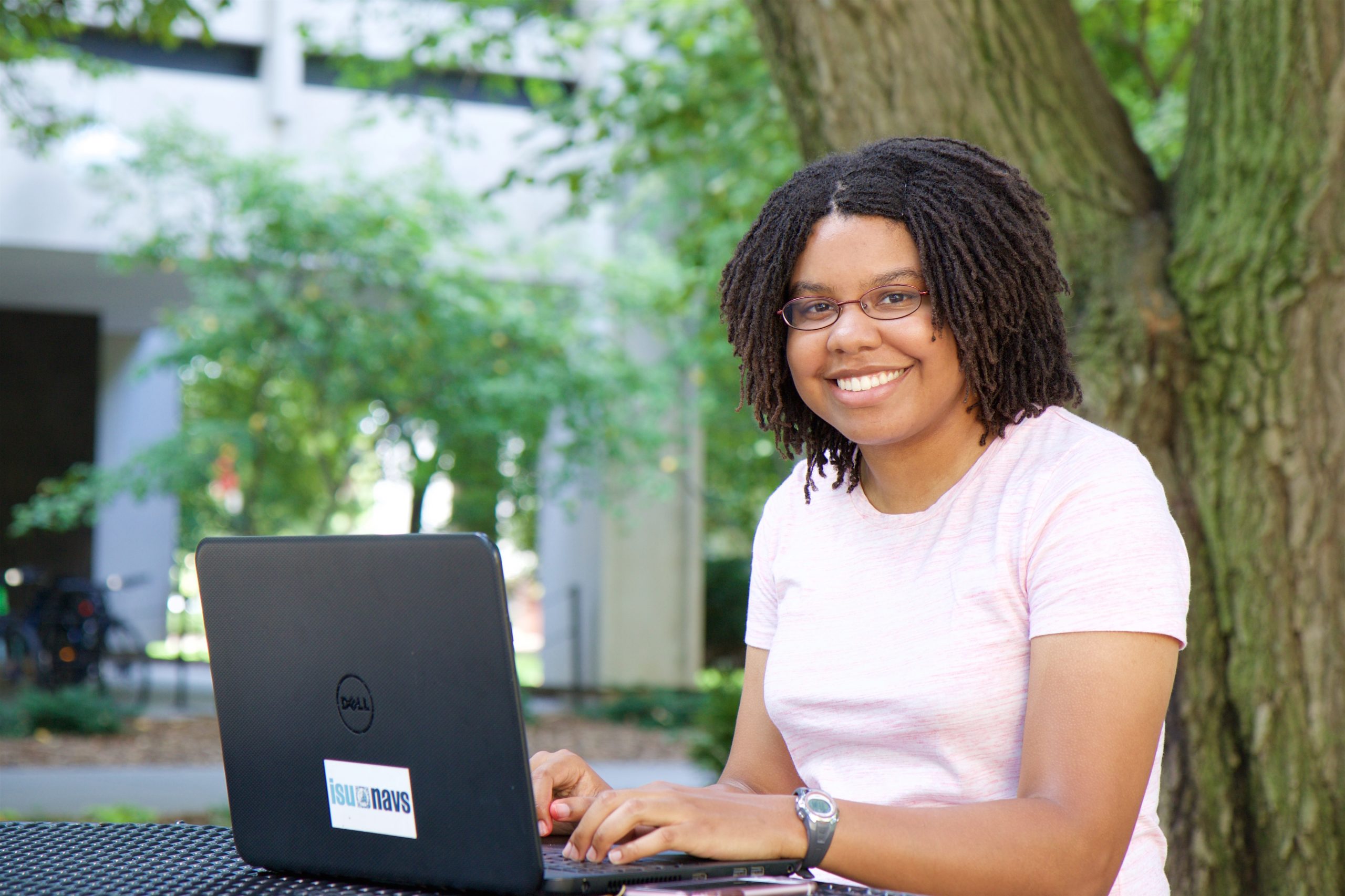 Student Catherine Thompson studies outside on her laptop at a picnic table beneath the trees near Carver Hall.