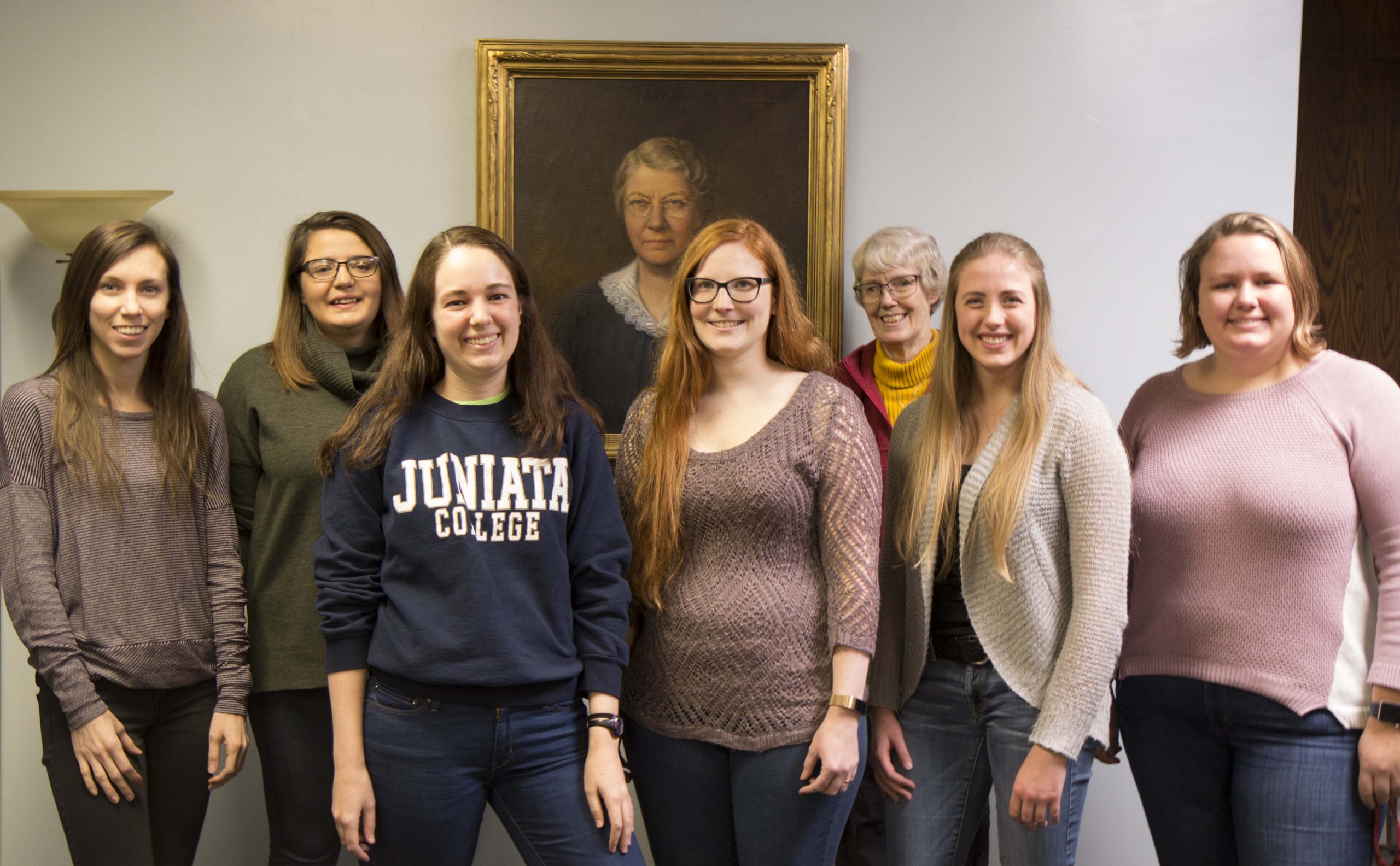 Graduate students and Leslie Hogben pose in front of a portrait.