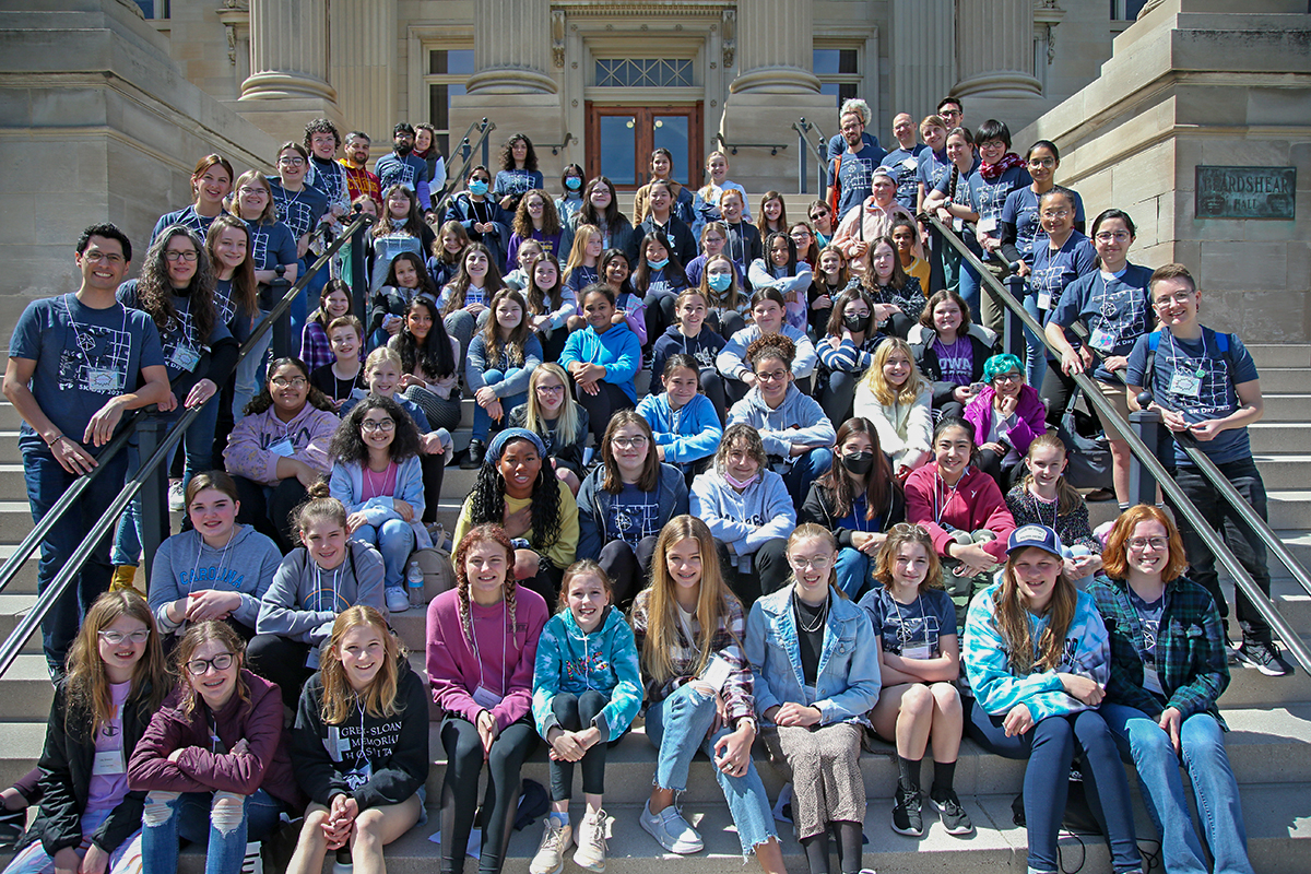 A large group of middle schoolers sits on the steps of Beardshear Hall