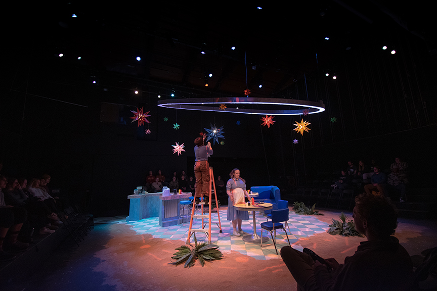 Actor on stage climbs a ladder to hang a light fixture