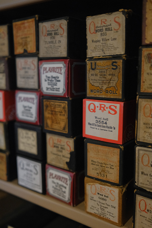 Player piano rolls stacked in their boxes on a shelf.