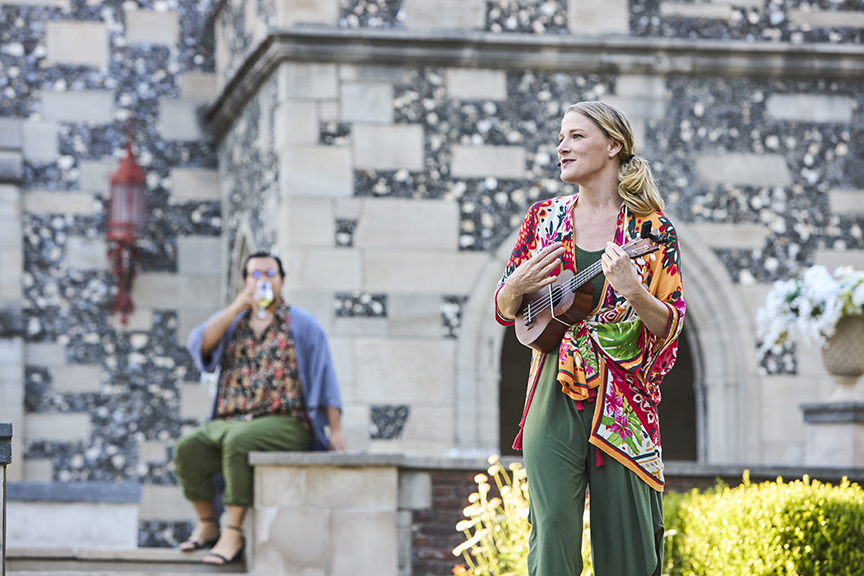 Actor performs with an instrument in King Lear outside historic house.