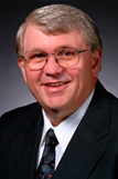 Man with gray hair and glasses in a suit.